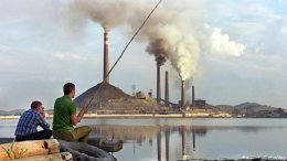 Two Russian men fish in a lake across from a factory